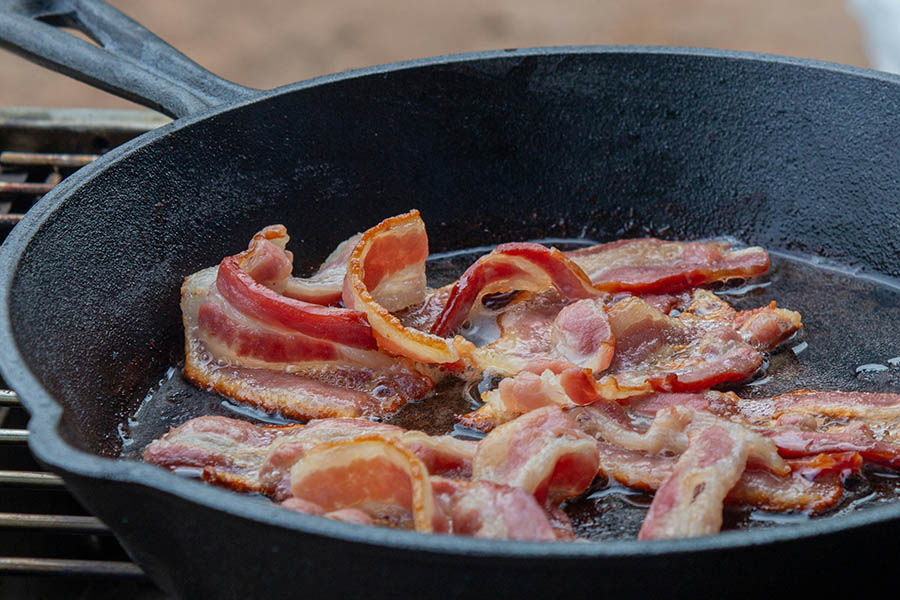 Pieces of bacon sizzling in cast iron skillet.